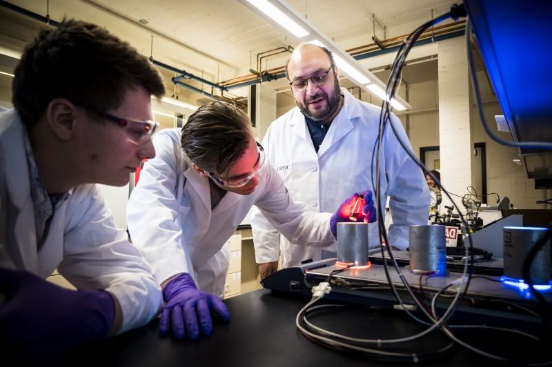 3 people in white lab coats inspecting a vial in red light