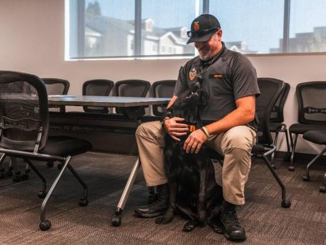 Cedar the dog sitting at a police officer's feet, looking up at him